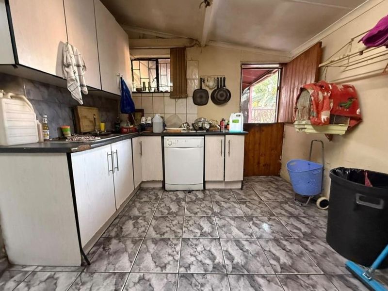 A functional kitchen featuring laminate cabinetry, tiled flooring, and direct access to the exterior via a timber door.