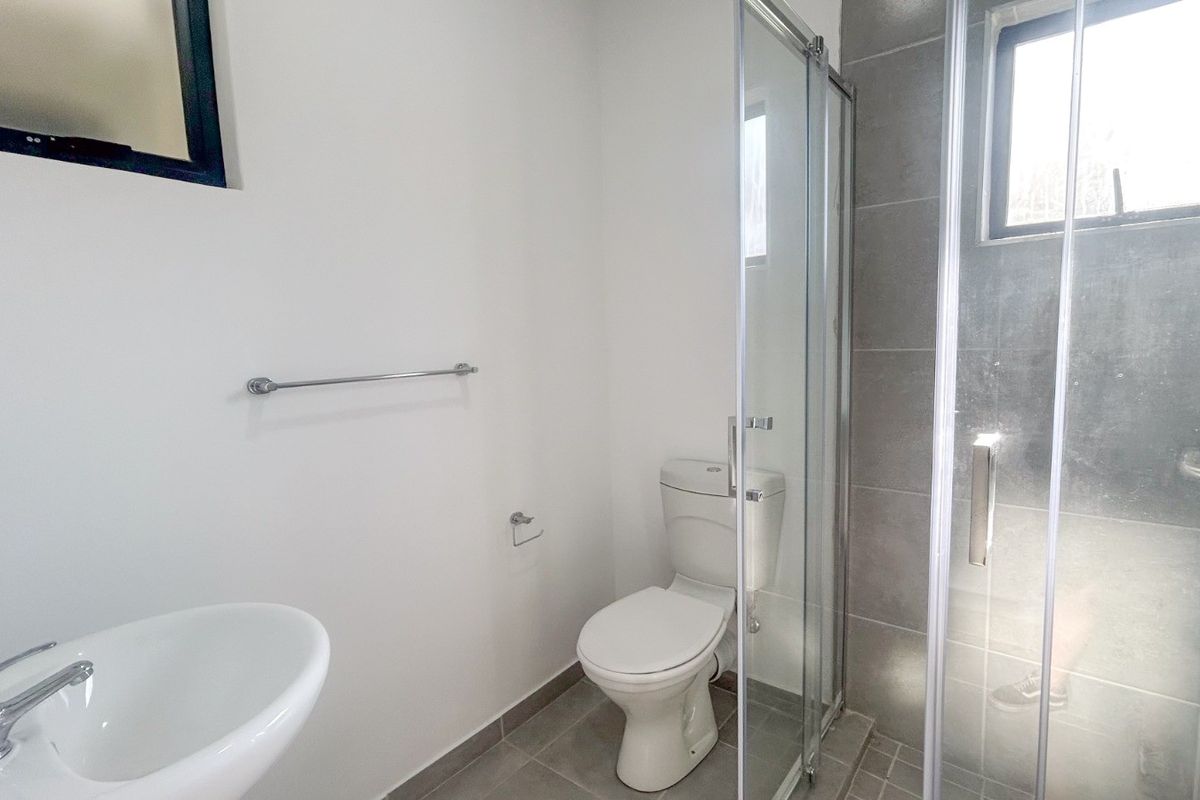 A clean, modern bathroom featuring a pedestal basin, toilet, and a glass-enclosed shower with grey tiled finishes.