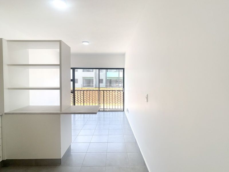 An open-plan living and kitchen area featuring tiled floors, modern built-in cabinetry, and a sliding door leading to a balcony.