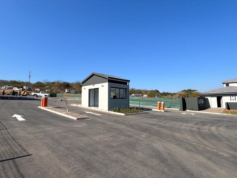 The entrance to the apartment complex features a modern security guard house, paved driveway, and controlled boom gate access.