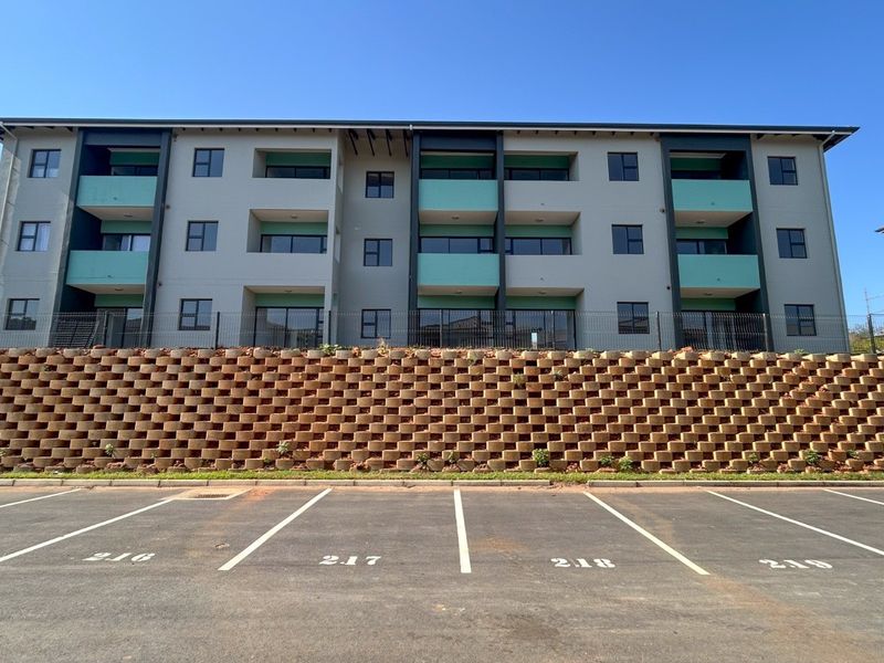 Front view of a modern apartment complex featuring designated parking bays and a large tiered retaining wall.