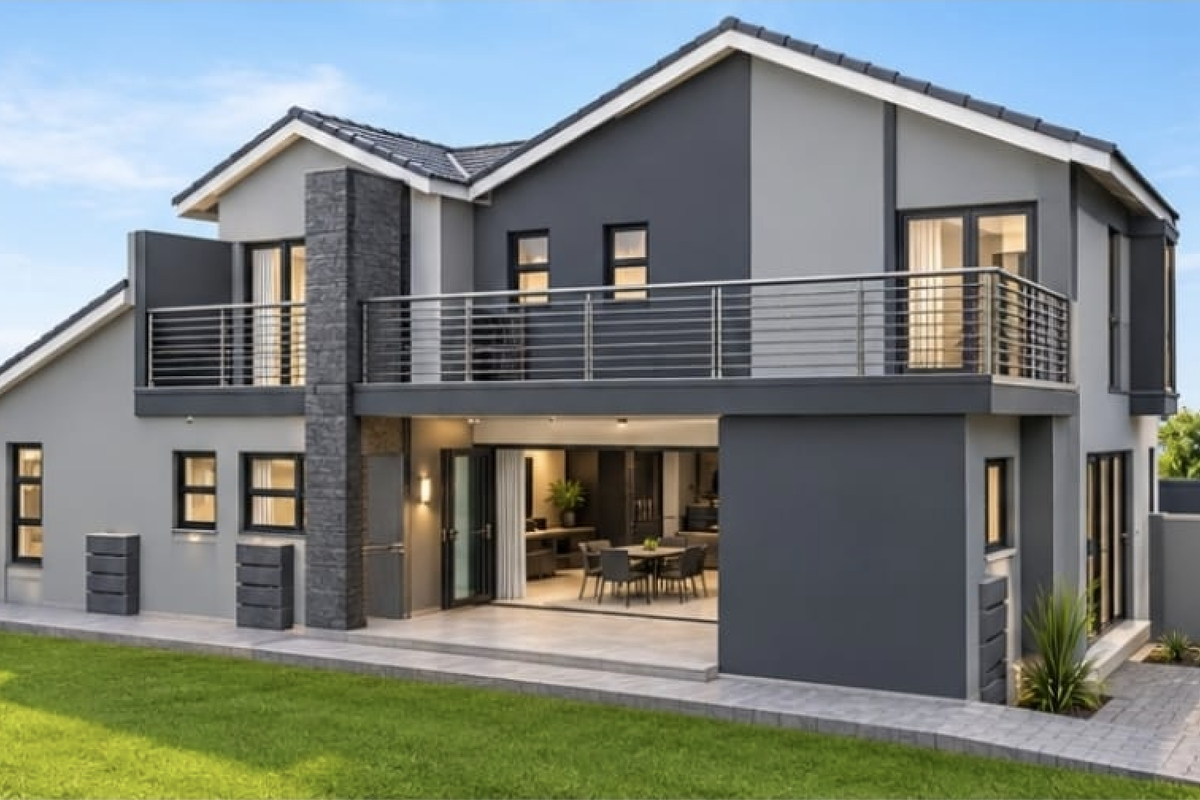 Modern double-story rear elevation featuring a spacious balcony, stone-clad chimney detail, paved patio area, and well-maintained landscaped garden.