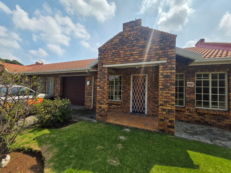 Front elevation of a face brick townhouse featuring a covered entrance, security gate, tiled roof, and an integrated garage with a roller door.