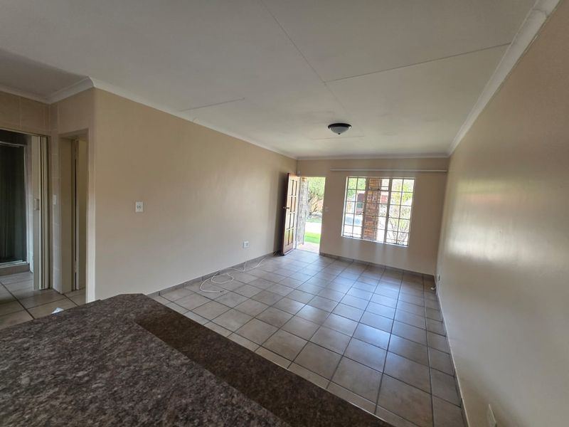 An open-plan living area featuring tiled flooring, coved ceilings, and direct access to the exterior, providing a blank canvas for interior design.