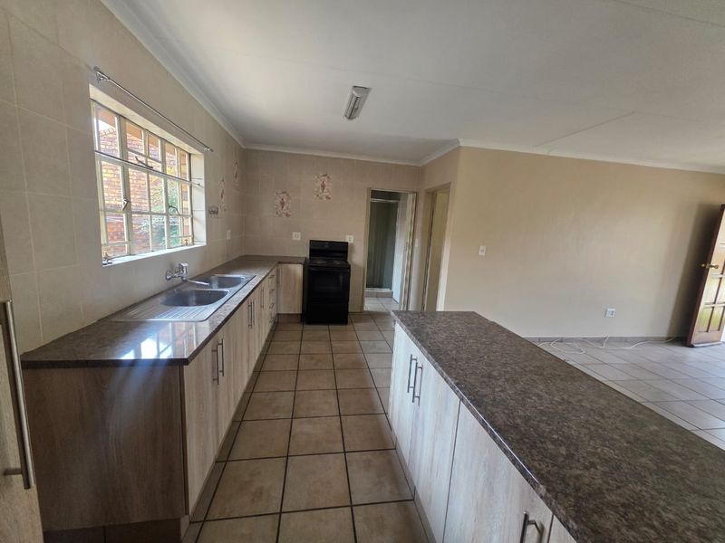 An open-plan kitchen featuring laminate countertops, built-in cabinetry, a double basin sink, and a freestanding stove, with neutral tiled flooring throughout.