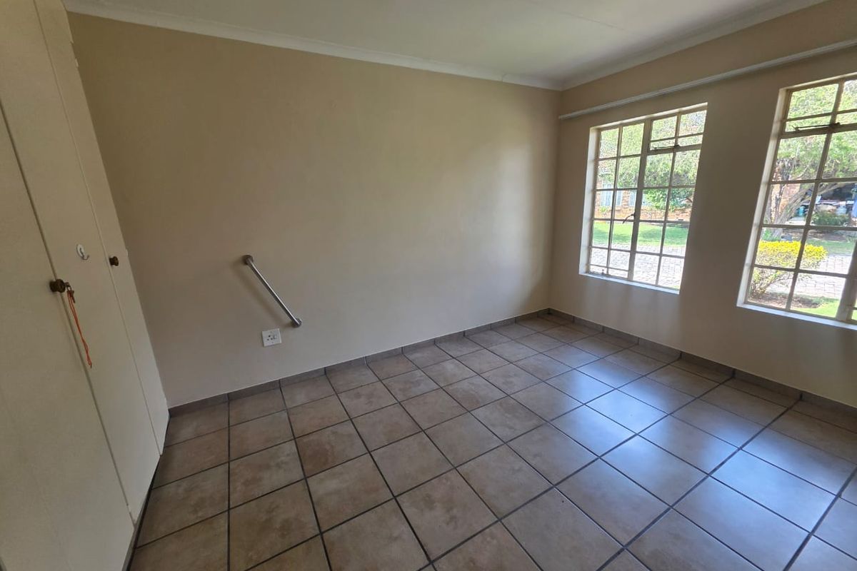 An empty bedroom featuring tiled flooring, built-in cupboards, and large steel-framed windows allowing natural light.