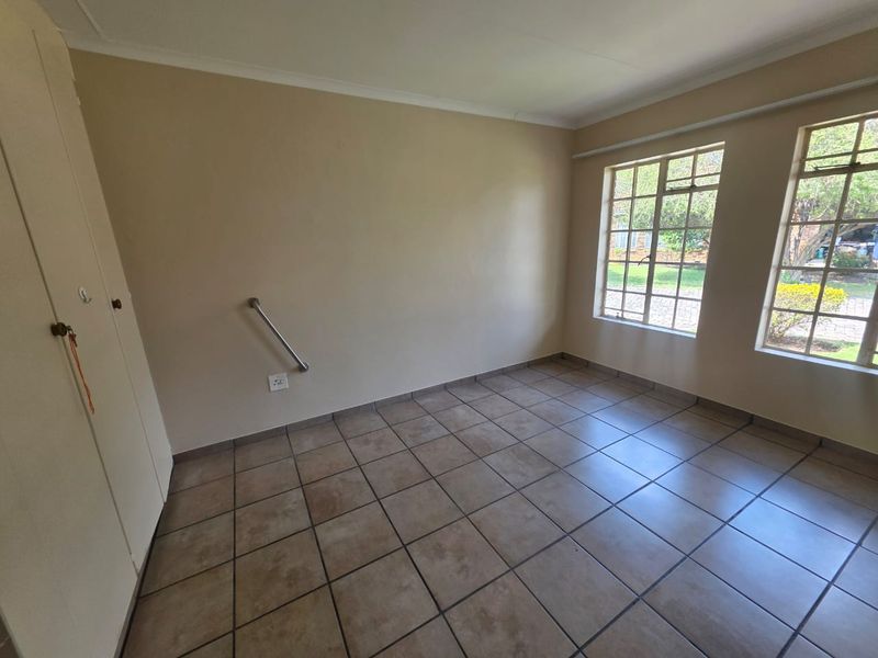 An empty bedroom featuring tiled flooring, built-in cupboards, and large steel-framed windows allowing natural light.
