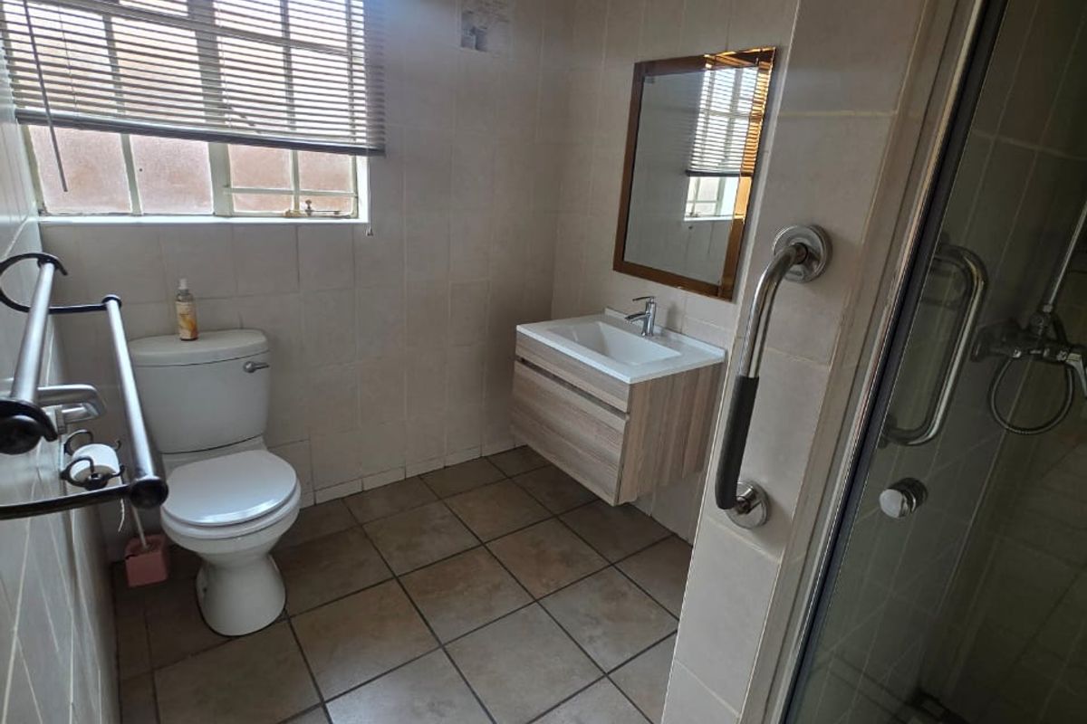 A functional bathroom featuring a wall-mounted vanity, a shower enclosure with a grab rail, and neutral tiled finishes throughout.