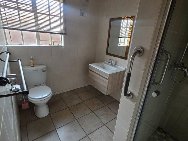 A functional bathroom featuring a wall-mounted vanity, a shower enclosure with a grab rail, and neutral tiled finishes throughout.