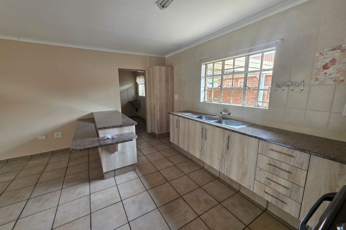 A functional kitchen featuring light wood-look cabinetry, laminate countertops, a double basin sink, and tiled flooring, with an adjoining breakfast bar area.