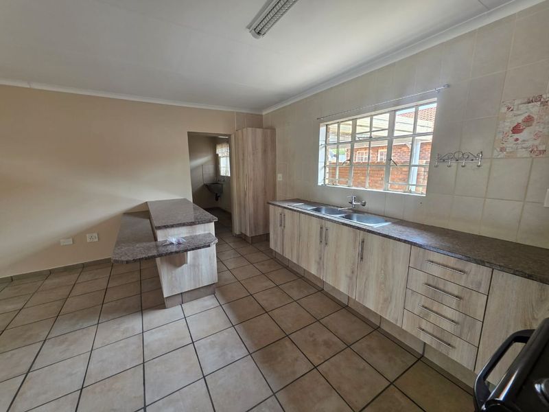 A functional kitchen featuring light wood-look cabinetry, laminate countertops, a double basin sink, and tiled flooring, with an adjoining breakfast bar area.