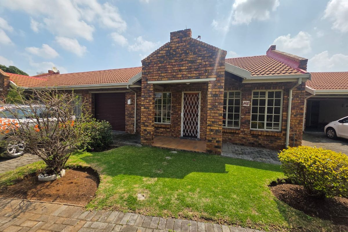 Front elevation of a face brick townhouse featuring a tiled roof, security entrance gate, paved driveway, and a well-maintained front garden.