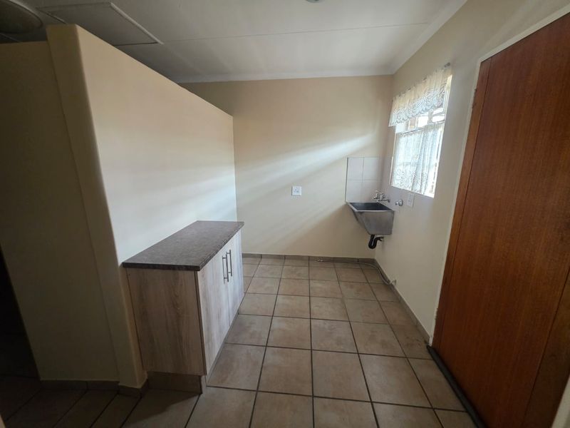 A functional laundry area featuring tiled flooring, a built-in utility sink, and additional storage cabinetry with a laminate countertop.