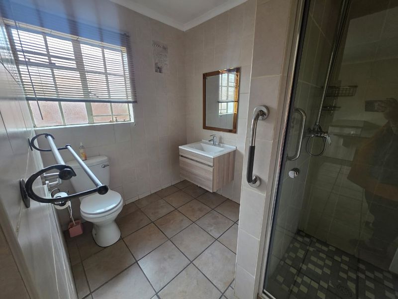 A functional bathroom featuring a glass shower enclosure, wall-mounted vanity, ceramic floor tiling, and neutral wall finishes.