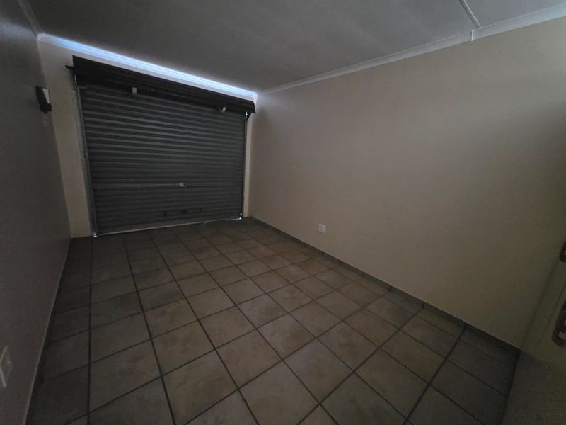 A clean, empty garage space featuring tiled flooring and a secure roller shutter door, offering versatile storage or parking potential.