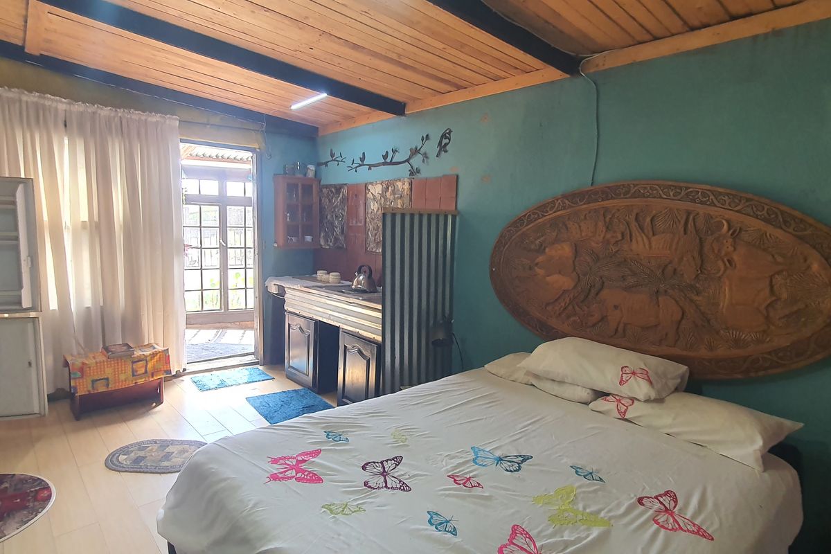 A rustic bedroom featuring an exposed timber ceiling, tiled floors, and a small integrated kitchenette area with direct access to the exterior.