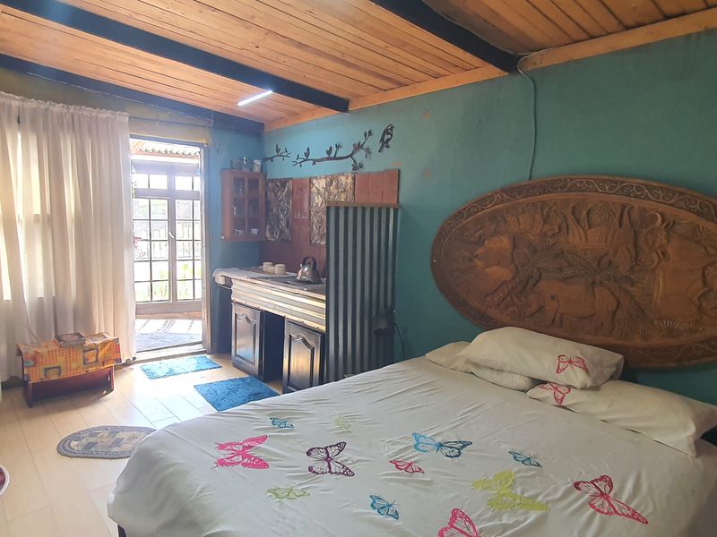 A rustic bedroom featuring an exposed timber ceiling, tiled floors, and a small integrated kitchenette area with direct access to the exterior.