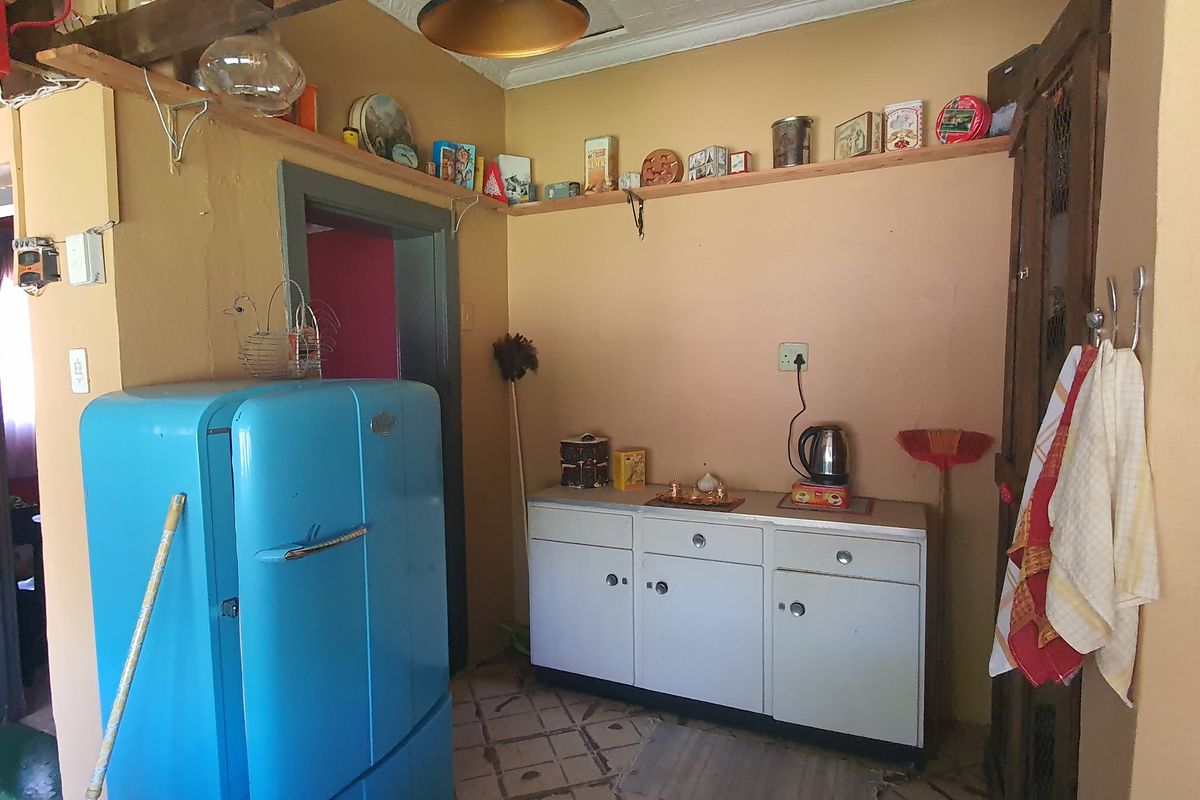 A dated kitchen area featuring built-in cabinetry, tiled flooring, and wall-mounted shelving, offering potential for a modern renovation.