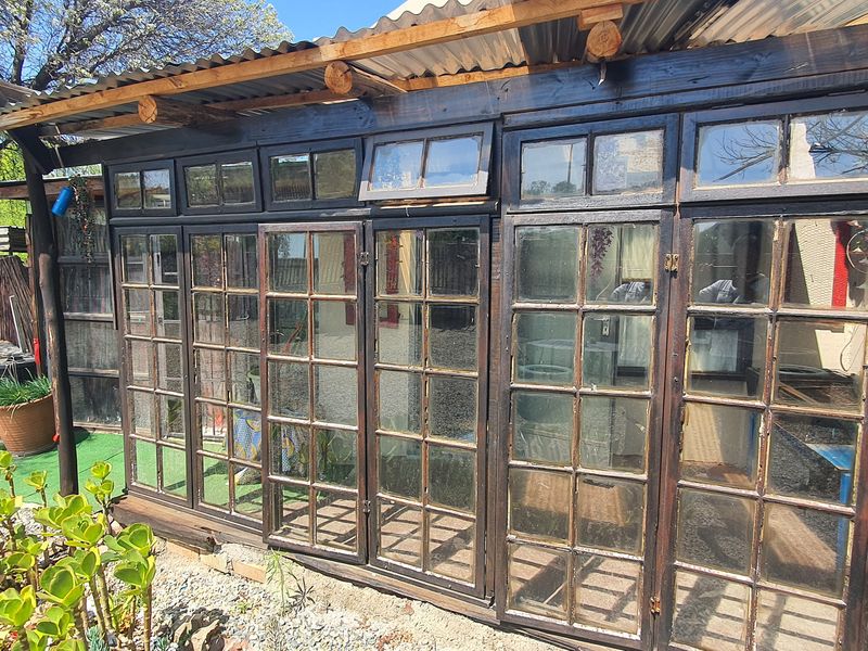 A rustic enclosed patio area featuring timber-framed glass doors and a corrugated iron roof, offering a potential space for outdoor living.