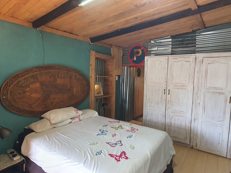 A rustic bedroom featuring an exposed timber ceiling, built-in wardrobe, and corrugated metal wall accents, requiring cosmetic updates to improve the overall finish.
