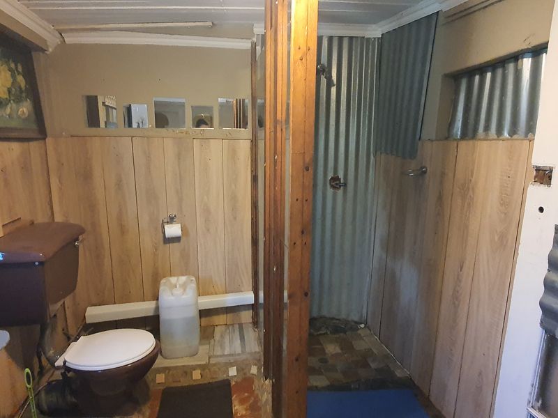 A dated bathroom featuring wood paneling, a corrugated metal shower enclosure, and basic sanitary fixtures in need of modernization.