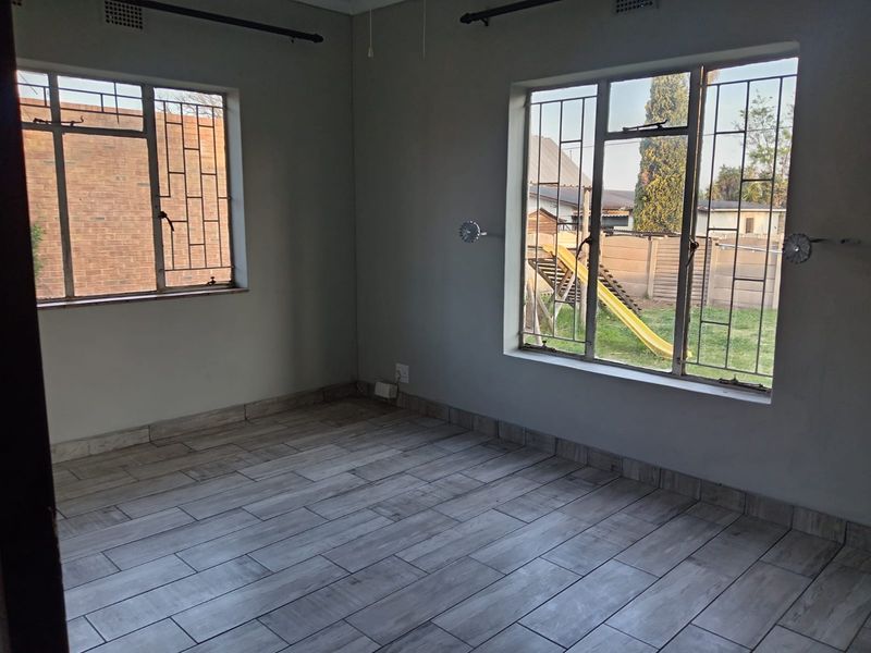 An empty bedroom featuring tiled flooring, security bars on the windows, and neutral wall finishes, offering a blank canvas for personalization.