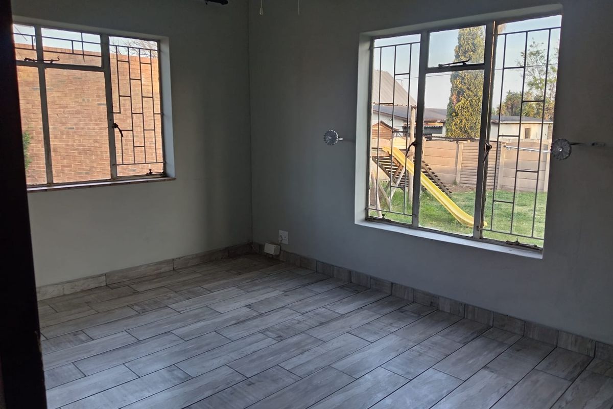 An empty bedroom featuring tiled flooring, security bars on the windows, and neutral wall finishes, offering a blank canvas for personalization.
