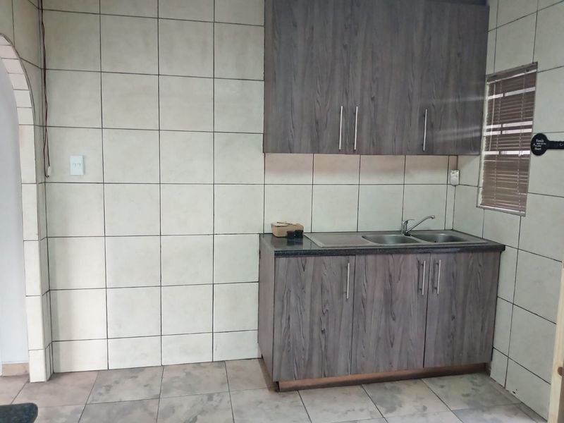 A functional kitchen area featuring dark wood-grain cabinetry, a double sink, and neutral tiled walls and flooring.