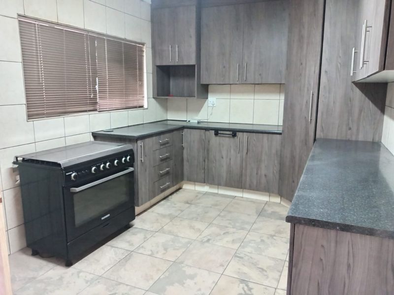 A functional kitchen featuring dark wood-look cabinetry, stone-effect countertops, tiled splashbacks, and a freestanding oven, offering a clean and practical workspace.