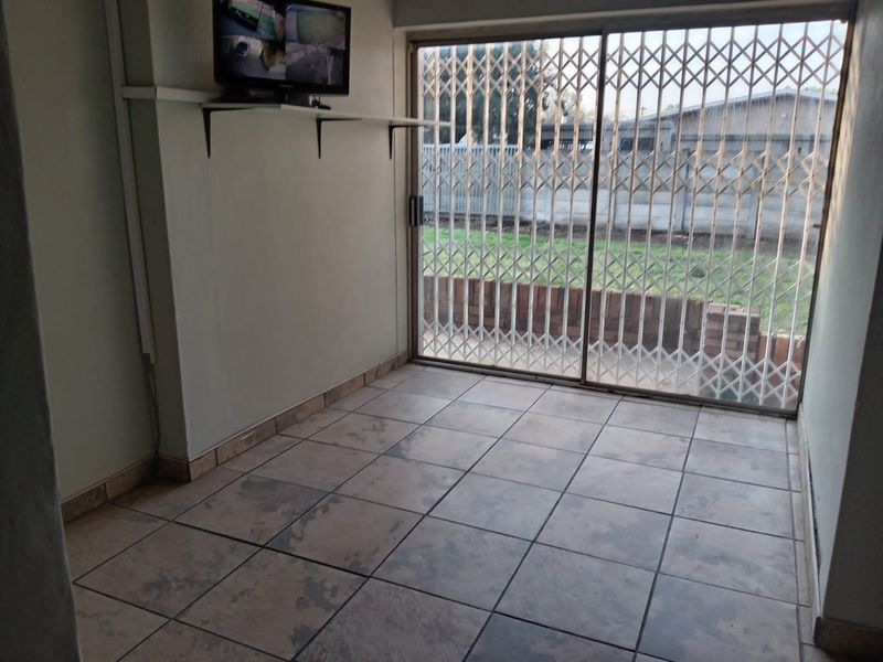An empty living area featuring tiled flooring and a sliding glass door with a security gate, providing direct access to the rear garden.