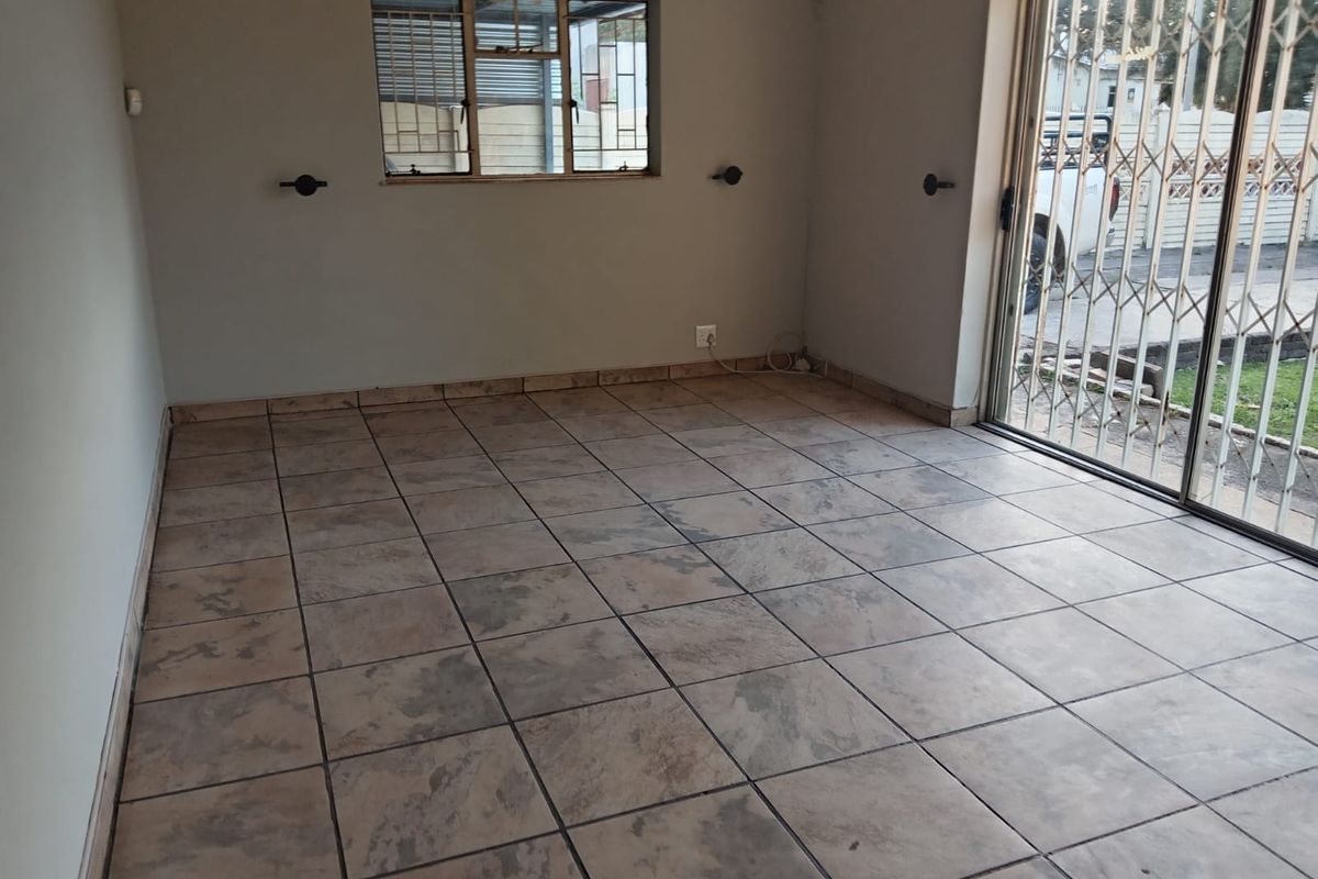 An empty living room featuring tiled flooring, a sliding glass door with security gate, and a window with security bars.