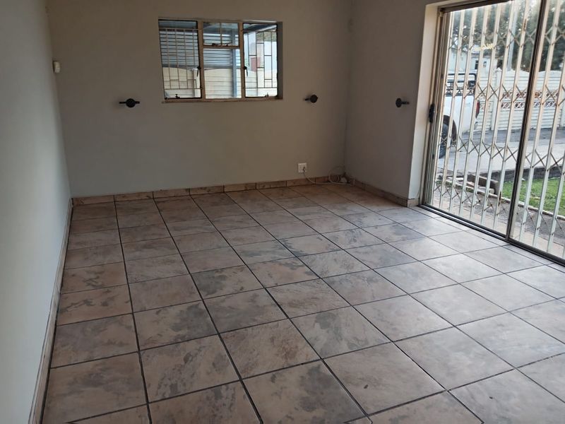 An empty living room featuring tiled flooring, a sliding glass door with security gate, and a window with security bars.