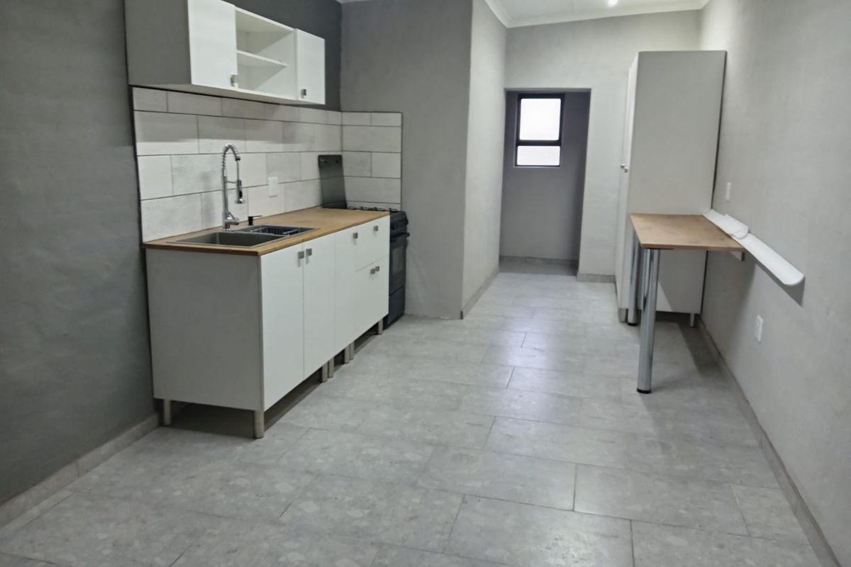 A clean, modern kitchen featuring white cabinetry, a tiled backsplash, stainless steel sink, and a wall-mounted breakfast bar with neutral tiled flooring.