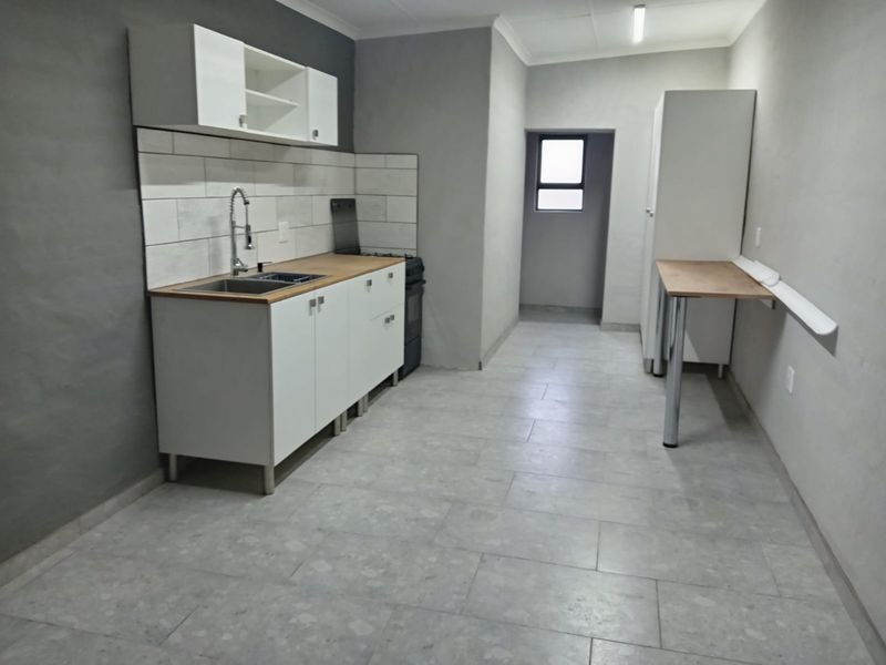 A clean, modern kitchen featuring white cabinetry, a tiled backsplash, stainless steel sink, and a wall-mounted breakfast bar with neutral tiled flooring.