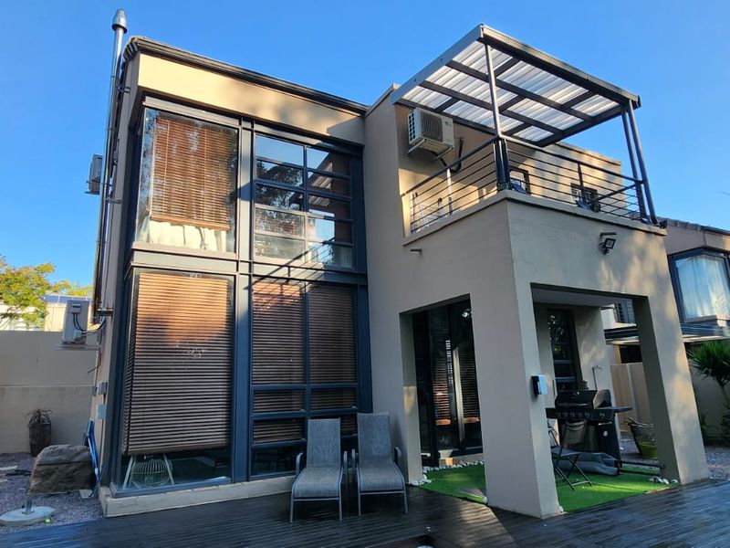 Rear elevation of a modern cluster home featuring double-volume windows, a covered patio with timber decking, and an upper-level balcony.