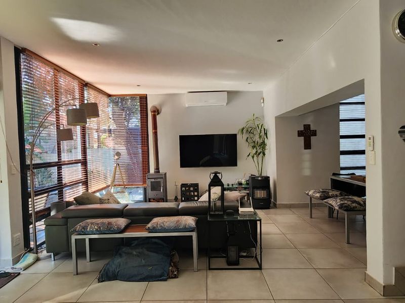 Spacious open-plan living area featuring tiled floors, a wood-burning fireplace, air conditioning, and large windows providing ample natural light and garden access.