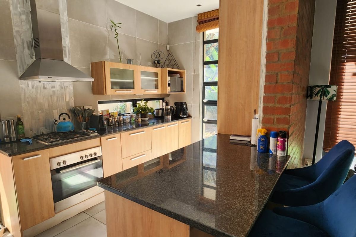 Modern kitchen featuring granite countertops, wooden cabinetry, built-in oven with gas hob, and a breakfast nook, complemented by an exposed brick feature wall.