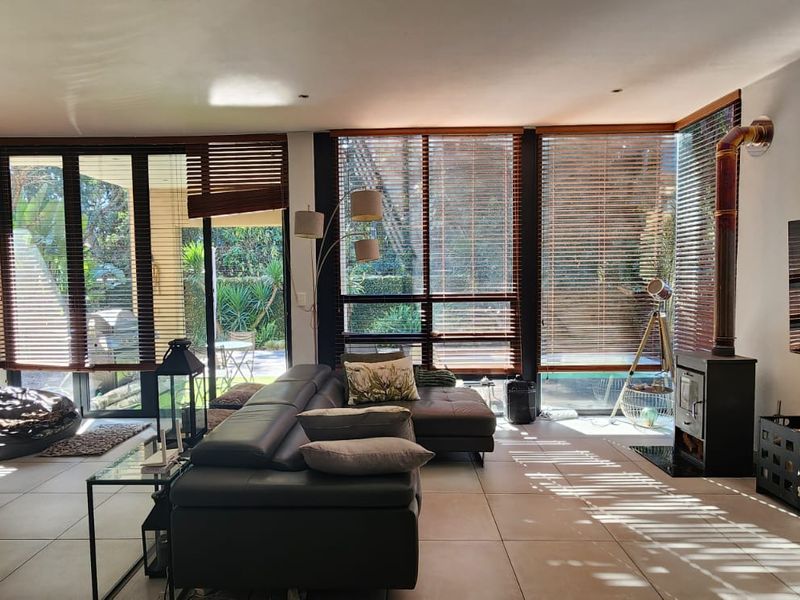 Spacious living room featuring an exposed brick feature wall, tiled flooring, a wood-burning fireplace, and large glass doors opening to the garden.