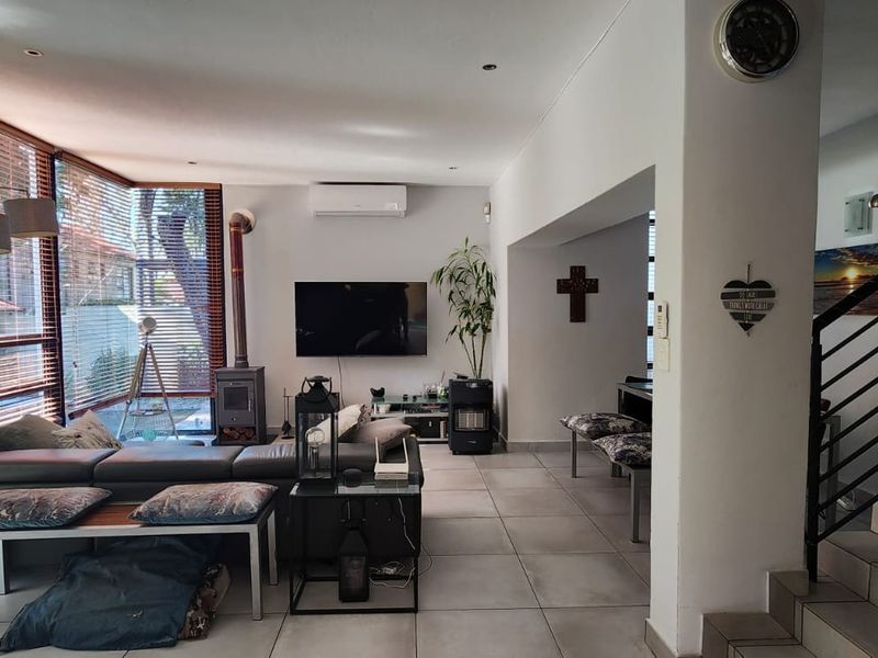 Spacious living area featuring large windows, tiled flooring, a wood-burning fireplace, and a modern staircase with a metal balustrade.