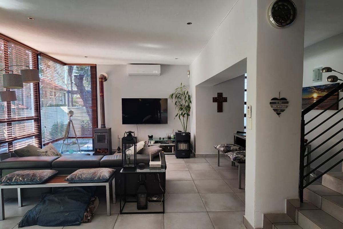Spacious living area featuring large windows, tiled flooring, a wood-burning fireplace, and a modern staircase with a metal balustrade.