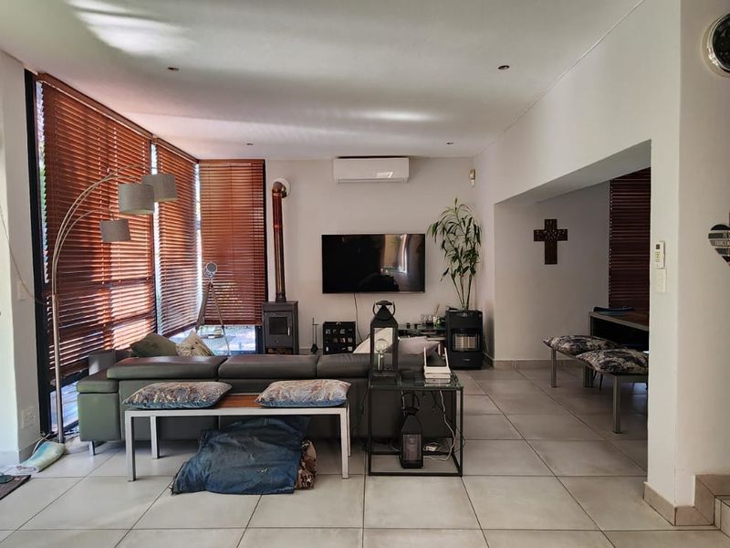 Spacious open-plan living area featuring large sliding glass doors, tiled flooring, a wood-burning fireplace, and an integrated staircase with modern metal railings.