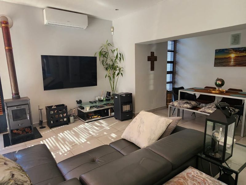 Open-plan living and dining area featuring tiled floors, a modern freestanding fireplace, and a wall-mounted air conditioning unit.