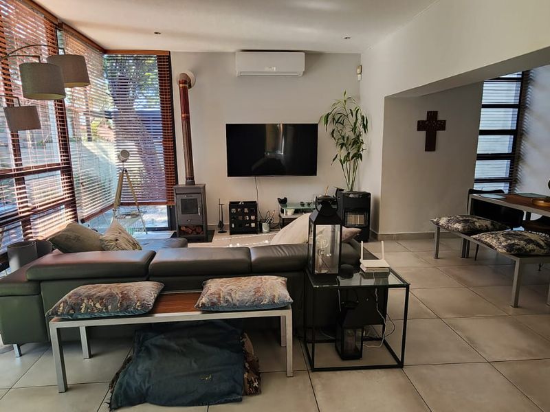 Spacious open-plan living and dining area featuring large windows, tiled floors, a wood-burning fireplace, and a wall-mounted air conditioning unit.