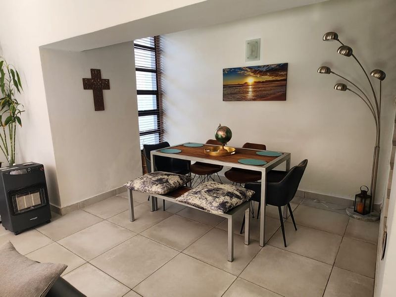 An open-plan living and dining area featuring tiled flooring, vertical blinds, and an integrated air conditioning unit, with a staircase leading to the upper level.
