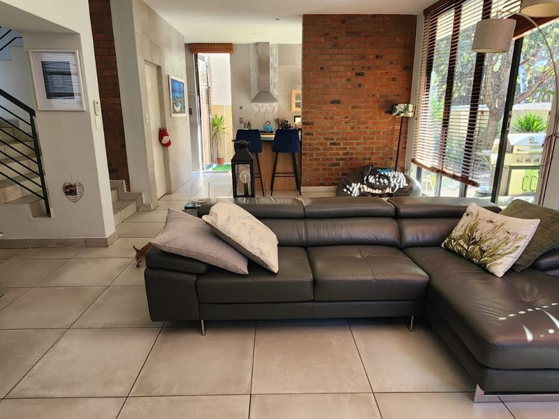 Spacious open-plan living area featuring modern tiled floors, an exposed brick feature wall, and a staircase, seamlessly flowing into the kitchen space.