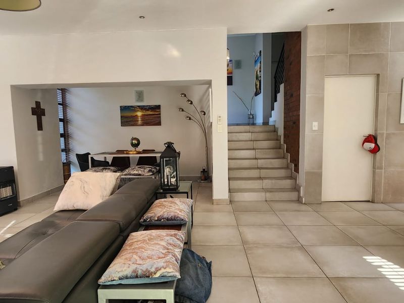 Spacious open-plan living area featuring large format floor tiles, a central staircase with exposed brick detailing, and a modern tiled feature wall.