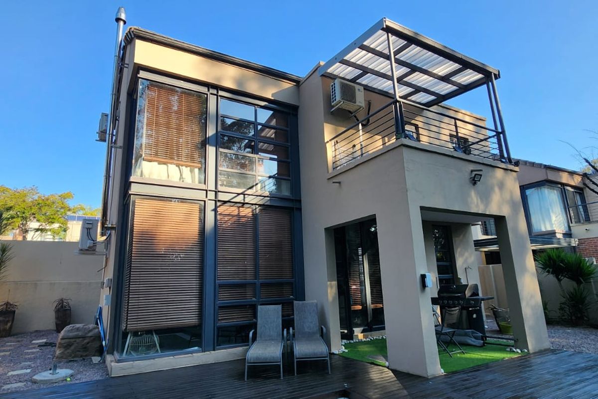 Rear elevation of a modern cluster home featuring double-volume windows, a covered patio with timber decking, and an upper-level balcony.