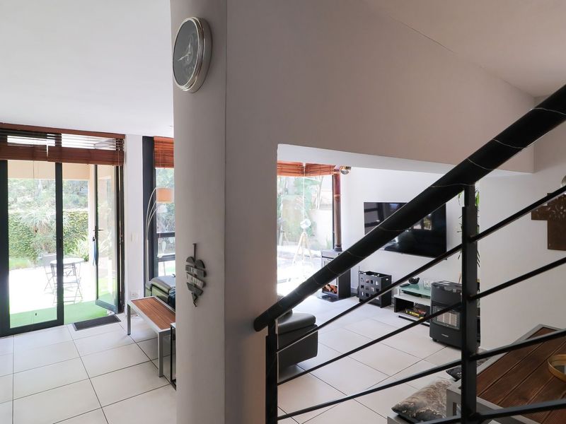 Open-plan living area featuring tiled floors, a modern staircase with metal balustrades, a freestanding fireplace, and large sliding doors opening to the garden.