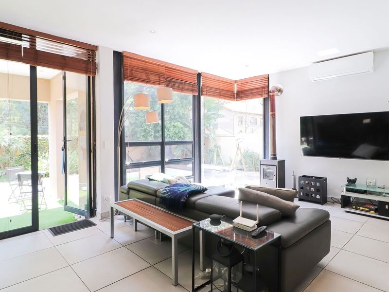 Bright and modern living room featuring large glass sliding doors, tiled flooring, a wood-burning fireplace, and a wall-mounted air conditioning unit.