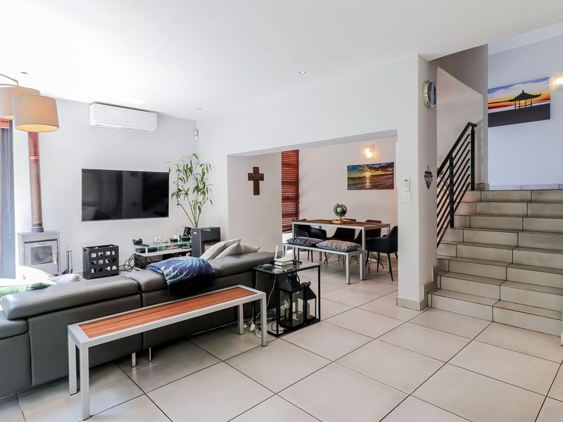 Spacious open-plan living and dining area featuring large format floor tiles, a modern wood-burning fireplace, split-system air conditioning, and a staircase with metal balustrades.
